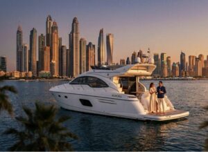 Sleek white luxury motor yacht cruising past the illuminated Dubai Marina skyscrapers at winter sunset, with a stylish couple enjoying champagne on the aft deck