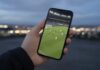 Hand holding a smartphone showing a blurred live sports stream